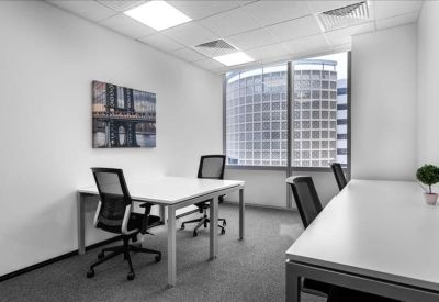 Private two-person office with white desks and a view of a neighboring glass skyscraper.
