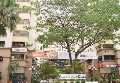 Outdoor pedestrian plaza with lush trees and ground-level retail storefronts.