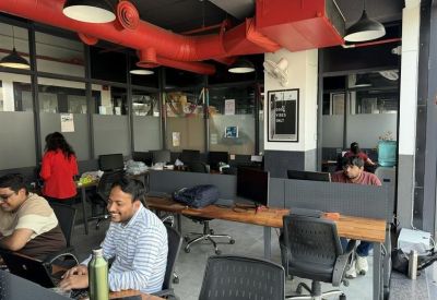 Open-plan workspace with industrial red ceiling ducts and people working at wooden desks.