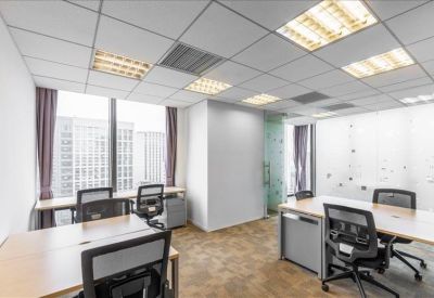 Bright corner office with wooden desks, black ergonomic chairs, and large windows.