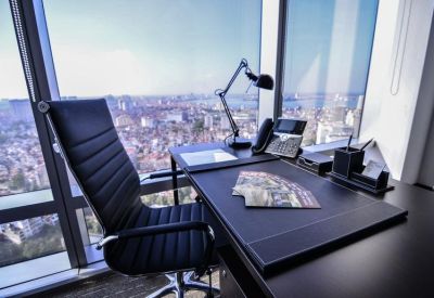 Private office with a black leather chair and a desk overlooking a vast cityscape.
