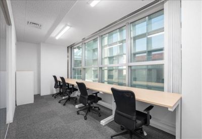 Bright coworking area with a long wooden desk facing large windows.