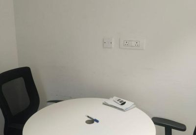 Small breakout area with a round white table and two black office chairs against a white wall.