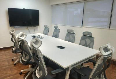 Bright conference room with a large white table, grey ergonomic chairs, and a wall-mounted screen.
