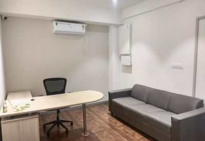 Private office suite with a curved desk, ergonomic chair, and a grey sofa.