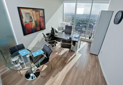 Executive office with a glass meeting table, abstract wall art, and light wood flooring.