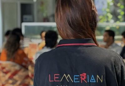 Staff member in a branded polo shirt standing in a busy, modern open-plan workspace.