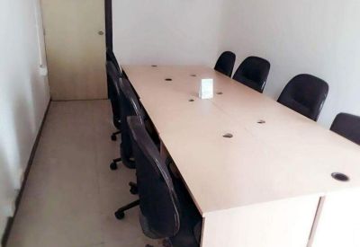 Internal long wooden desk with black office chairs in a simple room.