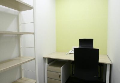 Private single-person office with a light green accent wall and tall white shelving unit.