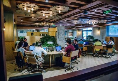 Coworking space with circular desks, indoor plants, and decorative gear-shaped ceiling lights.