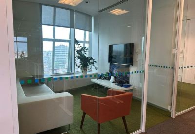 Lounge area with a grey sofa, orange armchair, and green carpet visible through glass.