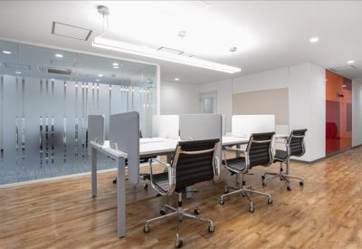 Bright common area with long white tables and ergonomic chairs on wood floors.