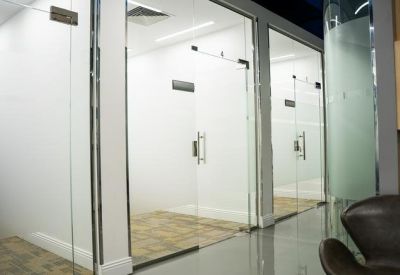 Glass-fronted private offices viewed from a polished grey hallway.