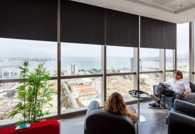 Spacious communal lounge area with armchairs, indoor plants, and floor-to-ceiling windows overlooking the coast.