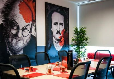 Meeting room featuring colorful portraits of famous authors, red placemats, and a long boardroom table.