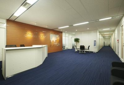 Spacious reception area with a white front desk, wood-paneled feature wall, and blue carpeting.