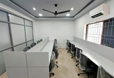 Modern open-plan workspace with multiple white desks, ergonomic chairs, and a ceiling fan.