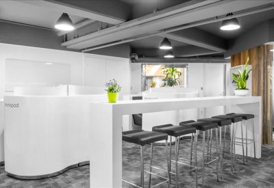 Sleek breakout area with high white bar table, stools, and exposed ceiling pipes.