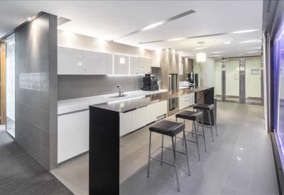 Sleek modern kitchen and break area with white cabinetry and black bar stools.