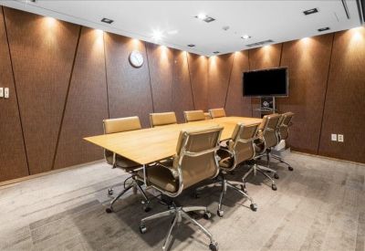 Professional boardroom with a long wooden table, leather chairs, and wall-mounted monitor.
