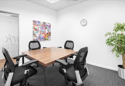 Bright four-person meeting room with a wooden square table and wall art.