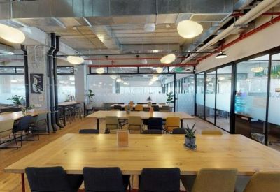 Open-plan office with large wooden communal workstations and glass-walled meeting rooms.
