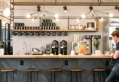 Modern office cafe bar with high stools, espresso machines, and industrial lighting.