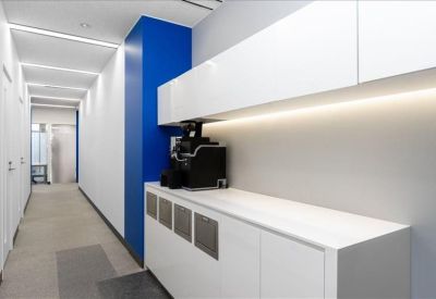 Kitchenette and breakout area with white cabinetry and a blue pillar along a bright hallway.