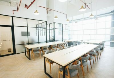 Bright workspace featuring long communal tables, ergonomic chairs, and glass-partitioned offices.