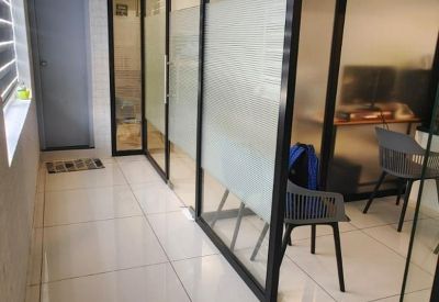 Modern office corridor with black-framed glass partitions and frosted privacy panels along a tiled floor.