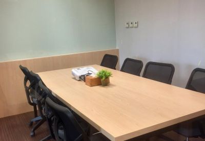 Six-person meeting room with a light wood table, black mesh chairs, and a white projector.