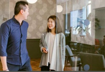 Colleagues walking and talking through a glass-walled corridor with natural light.