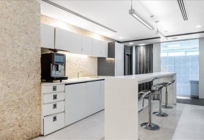 Modern communal kitchen with white cabinetry, a coffee machine, and breakfast bar stools.