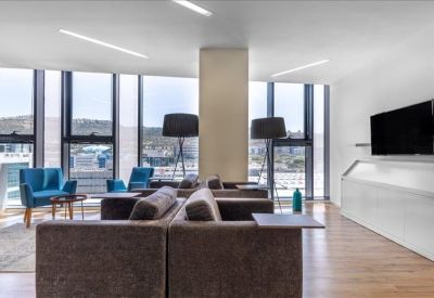 Spacious breakout lounge with brown sofas, blue armchairs, and floor-to-ceiling windows.