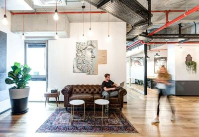 Leather sofa seating area with a patterned rug and wall art under industrial ceilings.