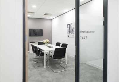 Professional meeting room with a white conference table, black chairs, and a glass door with frosted privacy film.