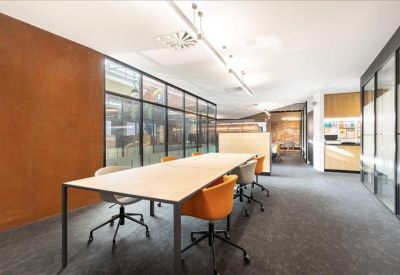 Bright coworking area featuring a long light-wood table and vibrant orange chairs.