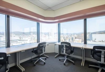 Bright corner workspace with panoramic city views and long desks paired with black office chairs.