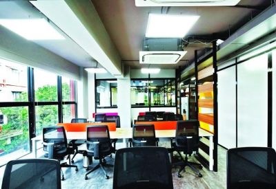 Open-plan workspace with rows of desks, black mesh chairs, and bright orange partitions.