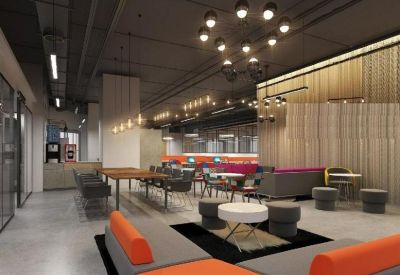 Spacious breakroom with orange L-shaped sofas, cafe seating, and industrial lighting.