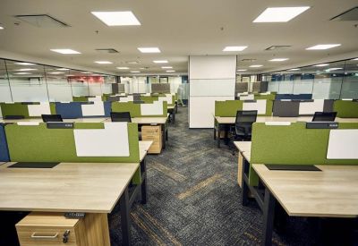 Open-plan office space featuring rows of desks with green privacy dividers and blue carpet.