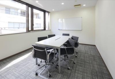 Sunlit meeting room with a white table, black chairs, and a whiteboard.