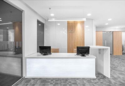 Minimalist white reception desk with two computer monitors and grey carpet.
