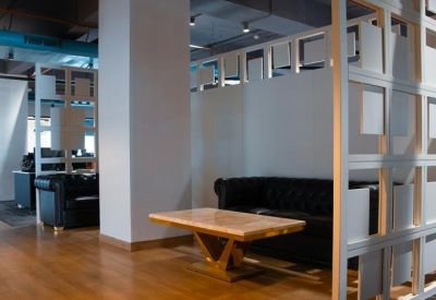 Cozy breakout area with a black leather sofa, light wood table, and decorative white partitions.
