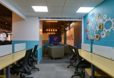 Modern coworking area with a creative lightbulb mural, wooden desks, and comfortable armchairs.