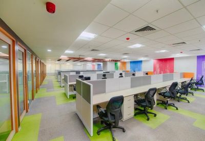 Open-plan office with rows of white cubicles, black chairs, and vibrant green and grey patterned carpet.