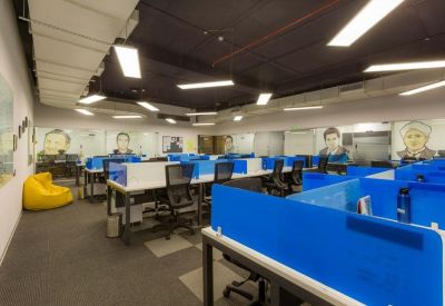 Open-plan office space with blue desk dividers, ergonomic chairs, and portraits on the walls.