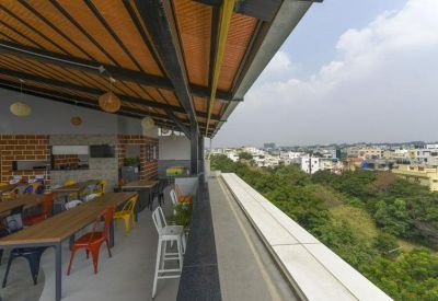Covered outdoor rooftop terrace with colorful seating and panoramic views of the city greenery.