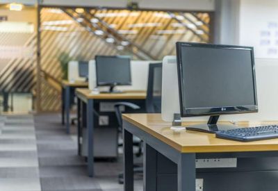 Row of modern wooden desks with computer monitors and ergonomic chairs.
