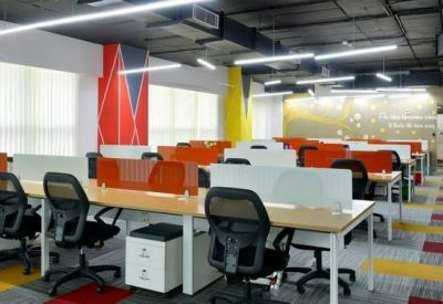 Bright open-plan office with colorful patterned carpet and rows of workstations with orange privacy screens.
